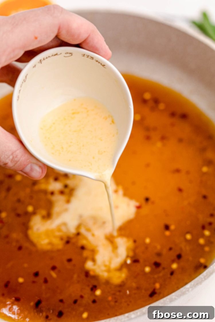 Cornstarch slurry being poured into a skillet with ingredients to make orange sauce.
