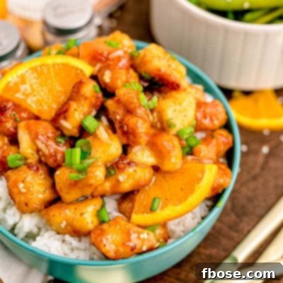 Close up photo of orange chicken on white rice in a teal bowl on a wooden table.