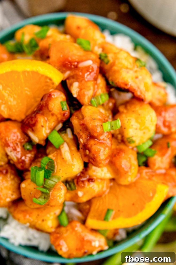 Close up photo of orange chicken on white rice in a teal bowl on a wooden table.