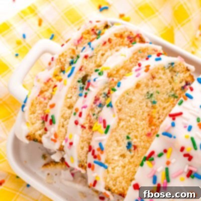 Close up photo of a slice of iced ice cream bread covered in rainbow sprinkles on a white plate on a yellow napkin.