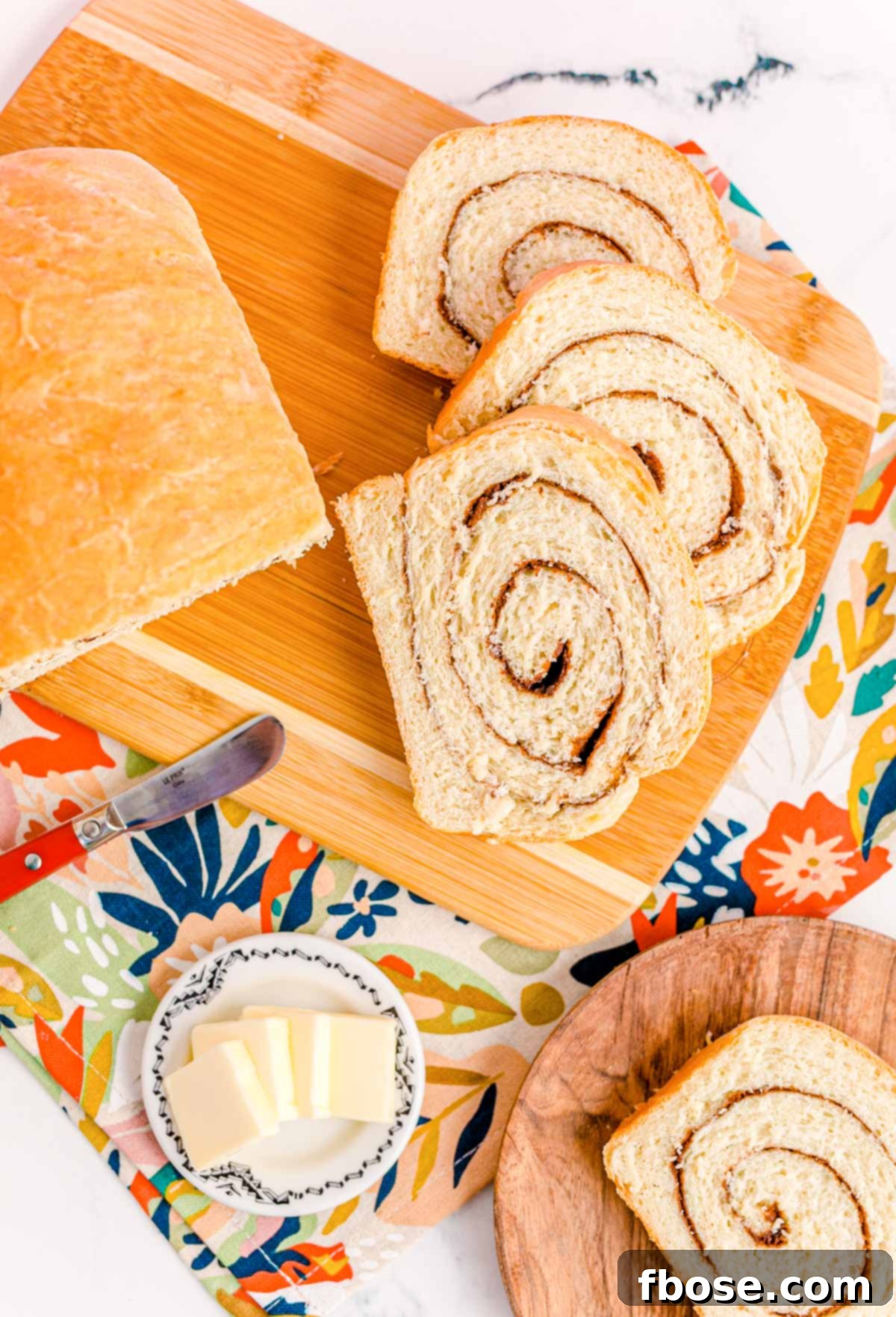 Overhead photo of a partial loaf and slices of cinnamon swirl bread on a cutting board on a floral napkin.