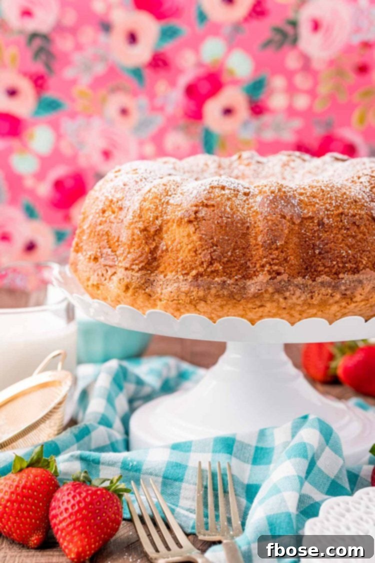 Cream Cloud Cake 3 Whipping cream cake on a white cake stand on a blue gingham napkin with a pink floral background. This simple, elegant cake is perfect for any occasion.