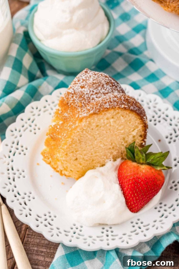 Cream Cloud Cake 6 A slice of whipping cream cake on a white plate with whipped cream and a strawberry on a teal gingham napkin. This is a perfect slice of a classic dessert.
