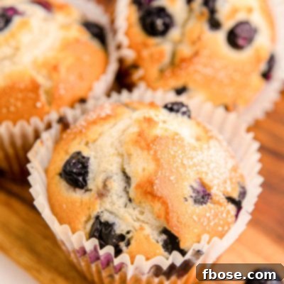 Bakery-Style Jumbo Blueberry Muffins 7 Three golden brown jumbo blueberry muffins sitting on a rustic wooden tray.