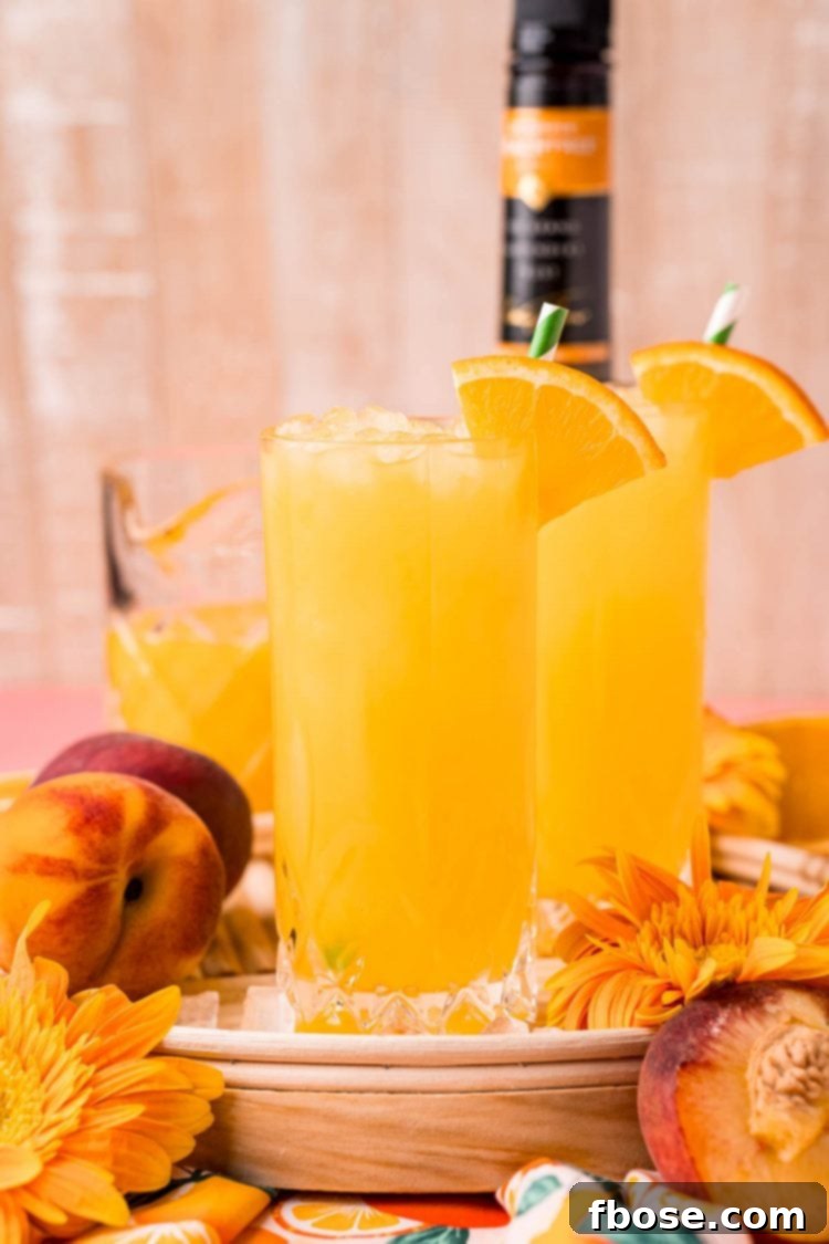 Close up photo of a glass filled with a fuzzy navel cocktail on a wooden serving tray, evoking a refreshing summer vibe.