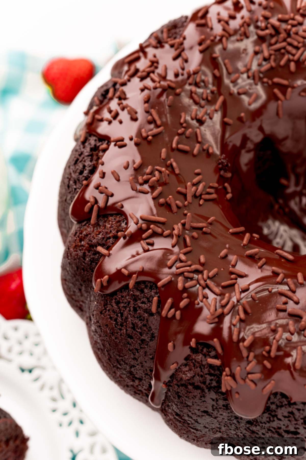 Angled photo of a beautifully garnished Devil's food bundt cake on a white cake stand, showcasing its rich texture and ganache topping.
