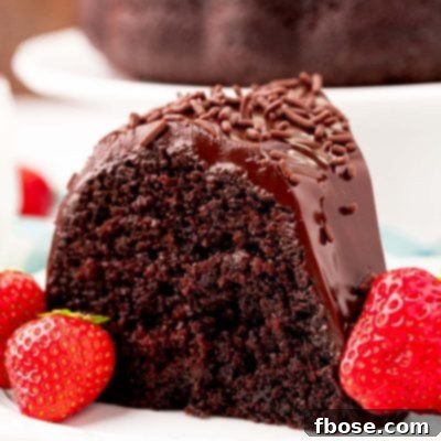 Close up photo of a slice of chocolate cake on a white plate with strawberries.