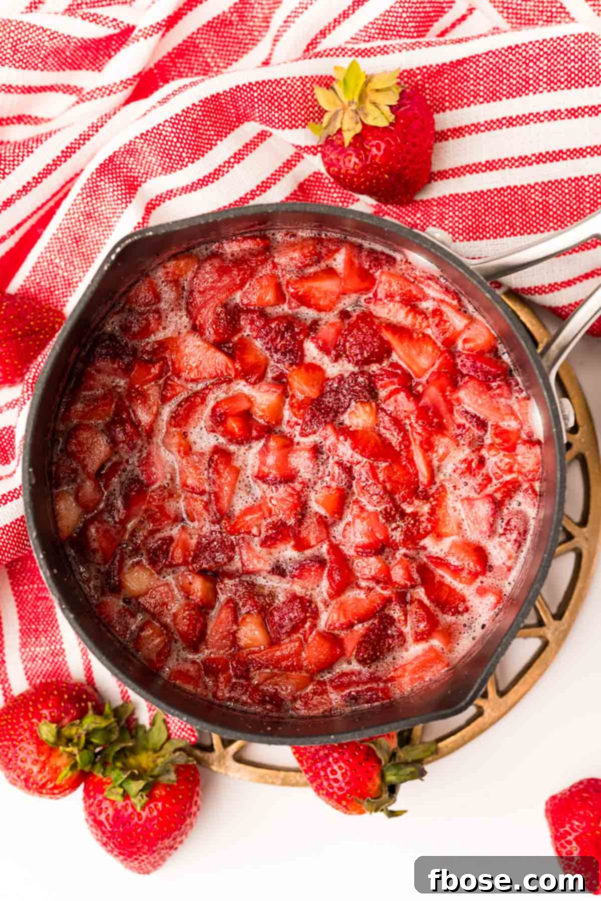 Overhead photo of a saucepan with sliced fresh strawberries and sugar, simmering to make strawberry simple syrup.