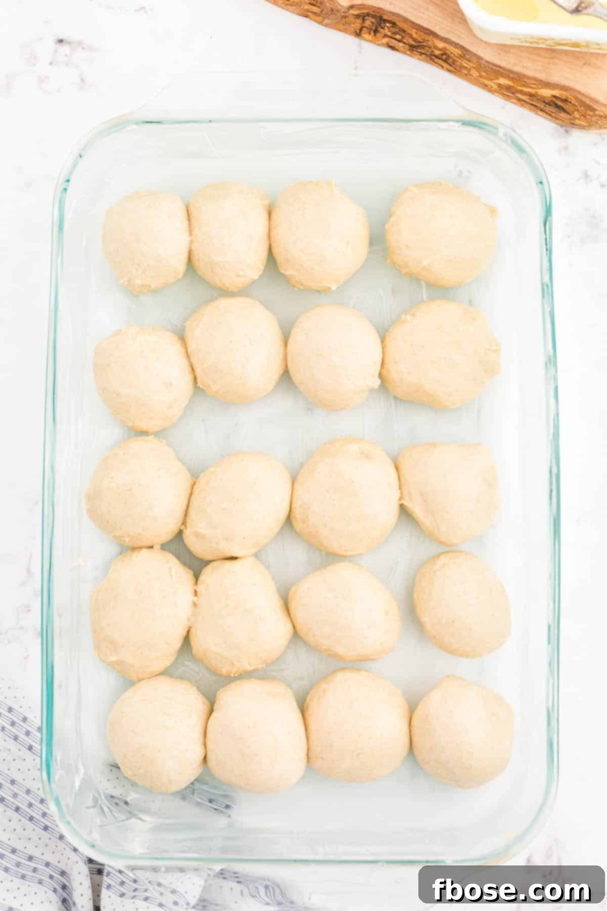 Unbaked balls of sourdough dinner roll dough neatly arranged in a buttered glass baking pan, ready for their second proof.