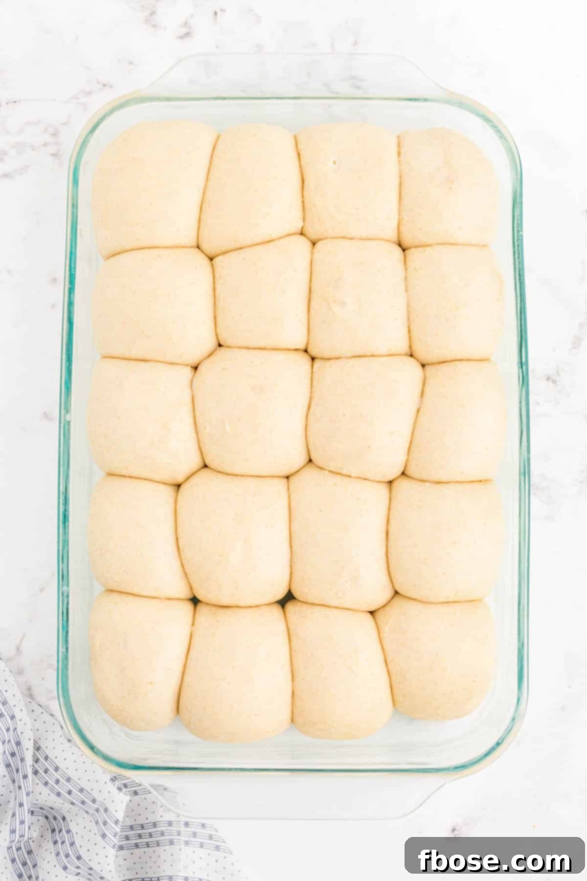 Fully proofed sourdough dinner roll dough, visibly expanded and touching each other, in a glass baking pan.