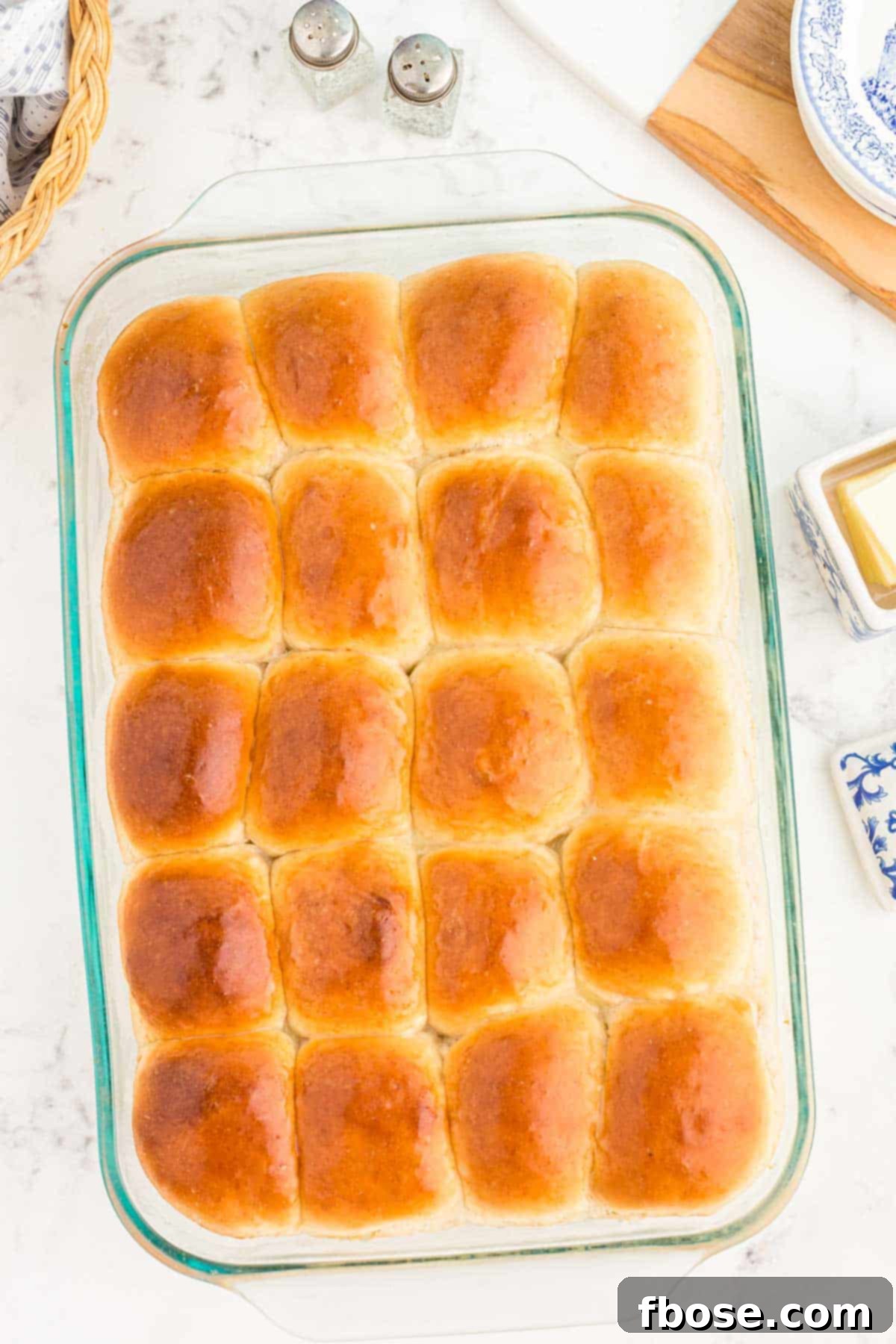 Overhead shot of a full pan of warm, golden-brown sourdough dinner rolls, glistening with melted butter brushed on top.