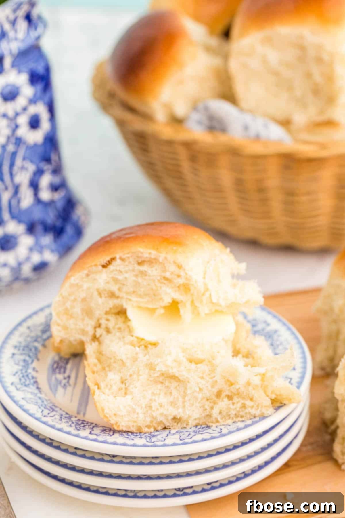 A single soft sourdough dinner roll resting on a stack of small white and blue ceramic plates, ready to be served.