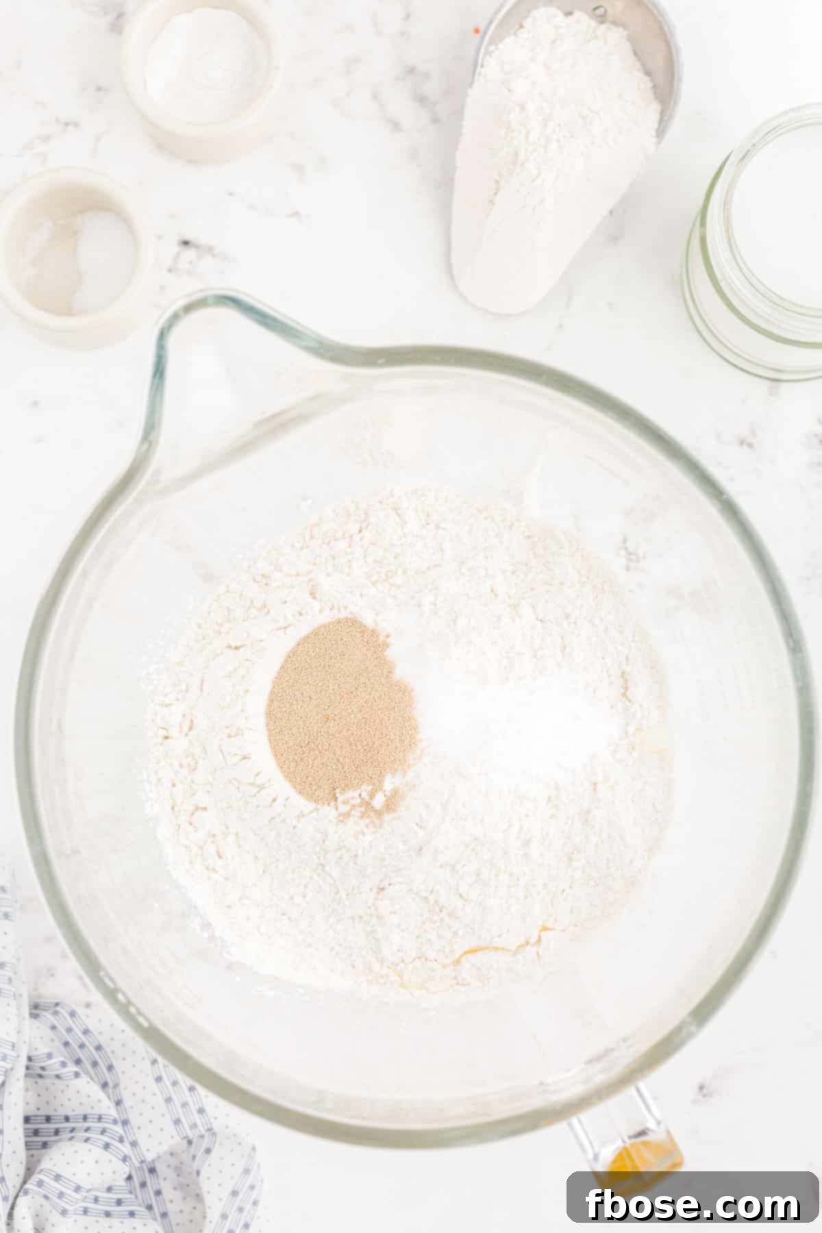 All-purpose flour, granulated sugar, sea salt, baking soda, and rapid-rise yeast layered over wet ingredients in a mixing bowl.