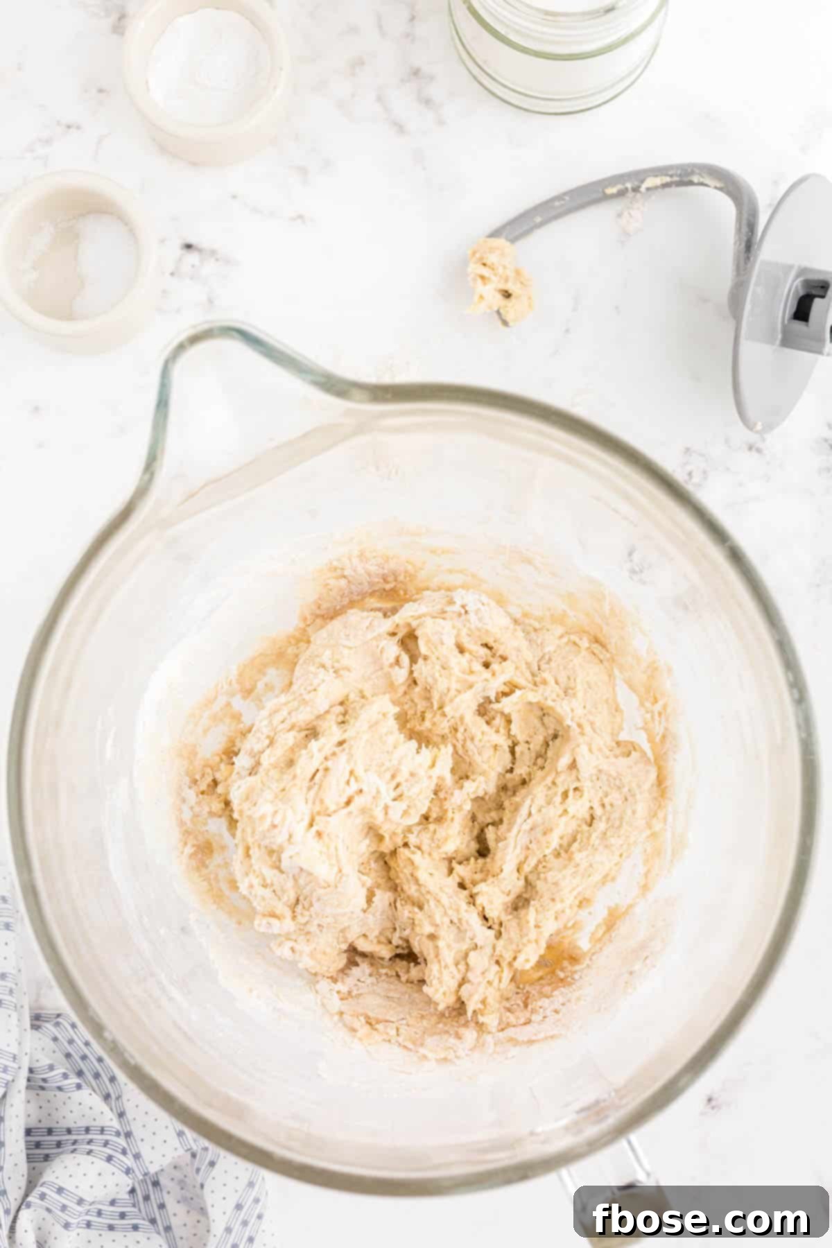 Shaggy dough for dinner rolls being mixed on low speed in a stand mixer with a dough hook.