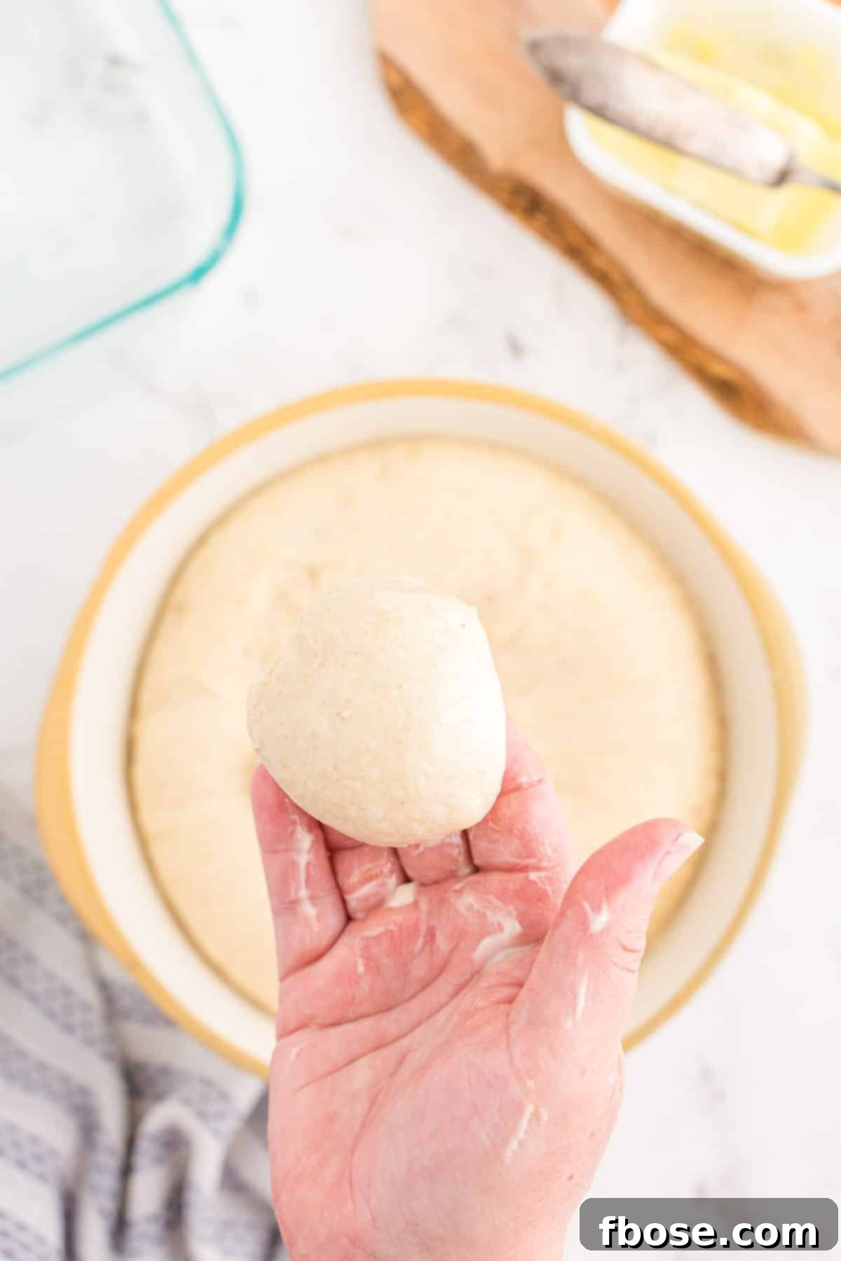 A woman's hand holding a perfectly rounded ball of sourdough dough, demonstrating the smooth top achieved through careful shaping.
