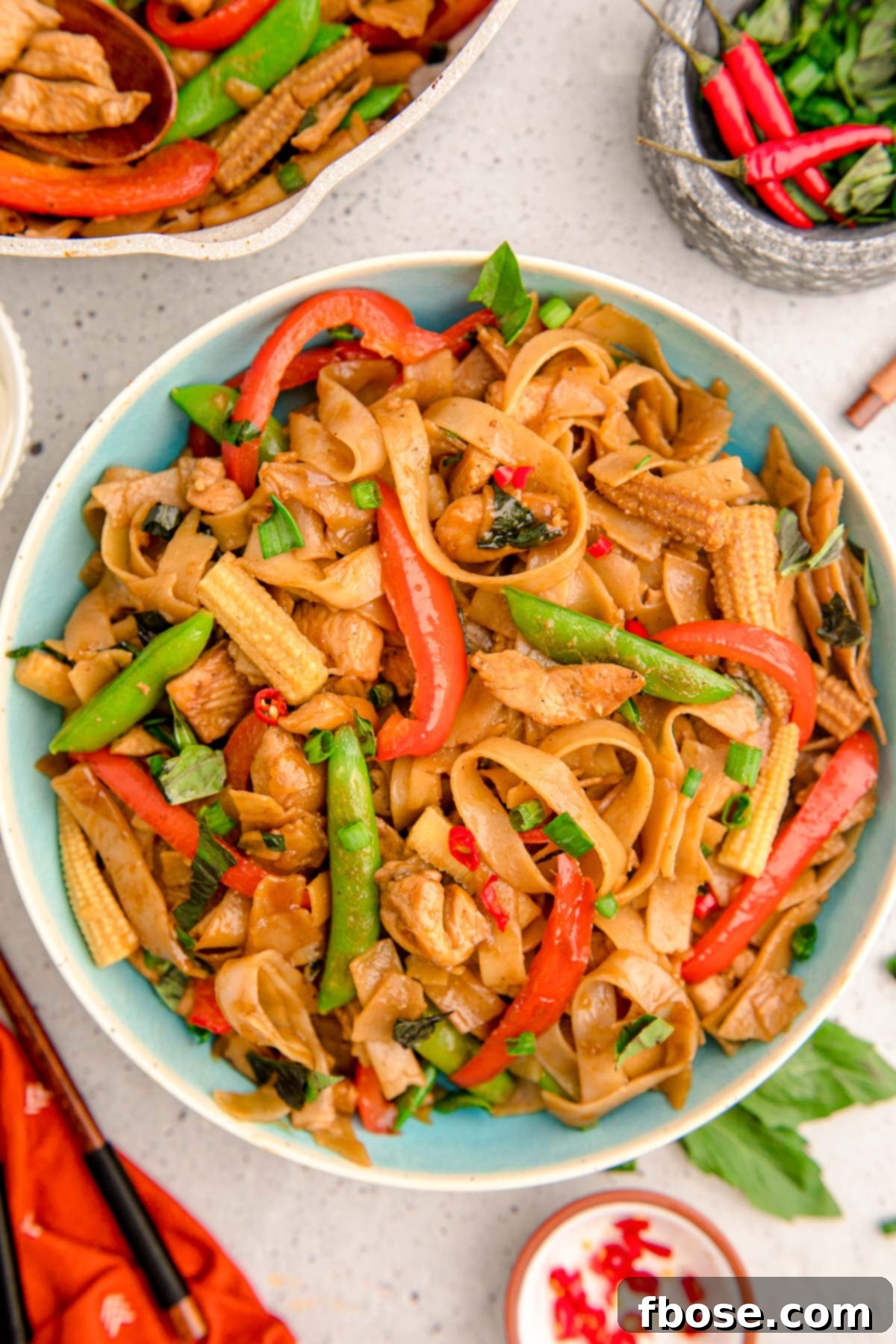 Overhead photo of a blue bowl filled with Drunken Noodles, showcasing a medley of noodles, chicken, and colorful vegetables.