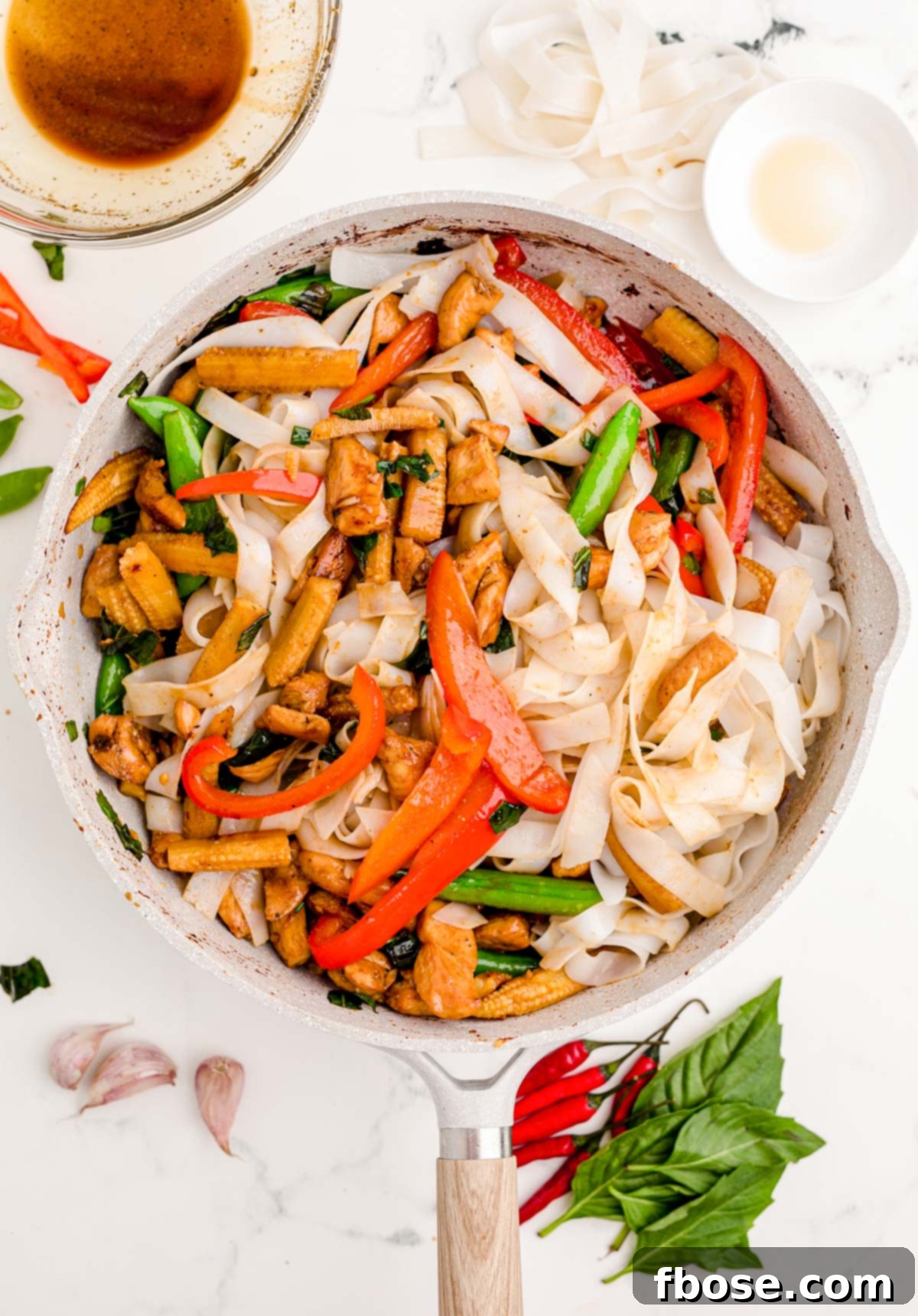 Drunken Noodles being tossed in a large skillet with all ingredients combined, absorbing the sauce.