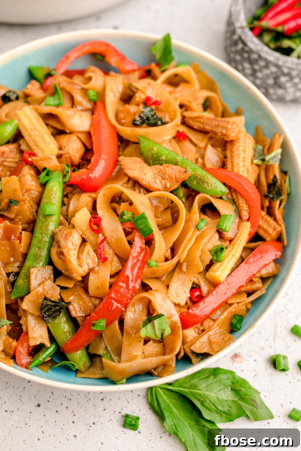 A beautiful blue bowl filled with Drunken Noodles, garnished with fresh herbs, on a wooden surface.