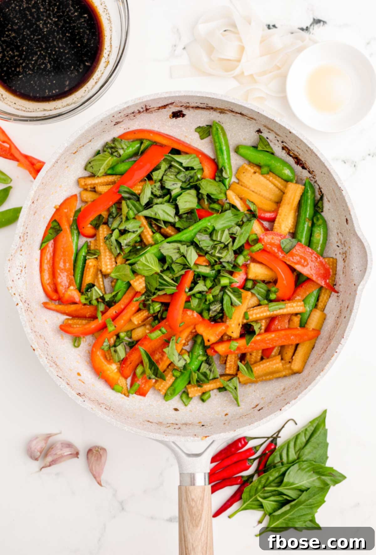 Fresh Thai basil and green onions being added to the stir-frying vegetables in a skillet.