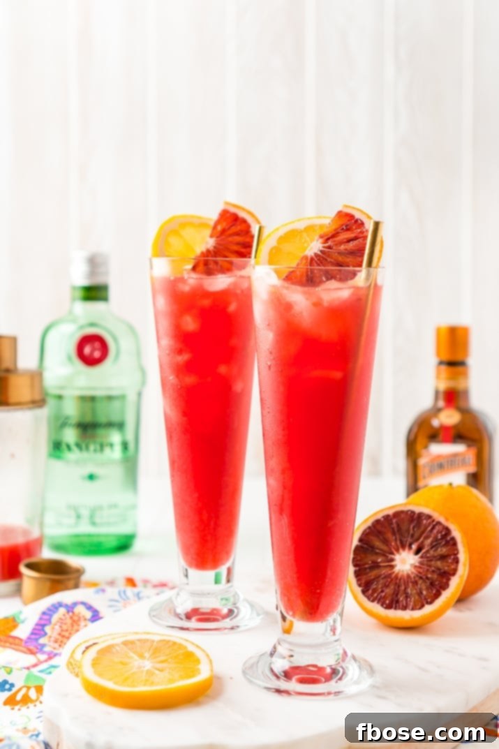 Two vibrant Blood Orange Cocktails sitting side-by-side on a dark surface, ready to be enjoyed.