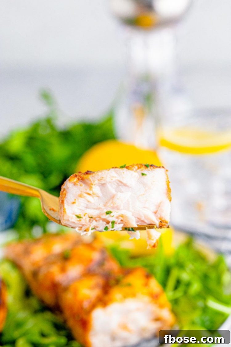 A fork holding a bite of mahi mahi fish above a plate.