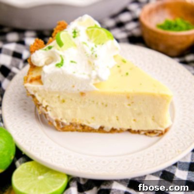 Close up photo of a slice of key lime pie on a white plate on a black and white checkered napkin.