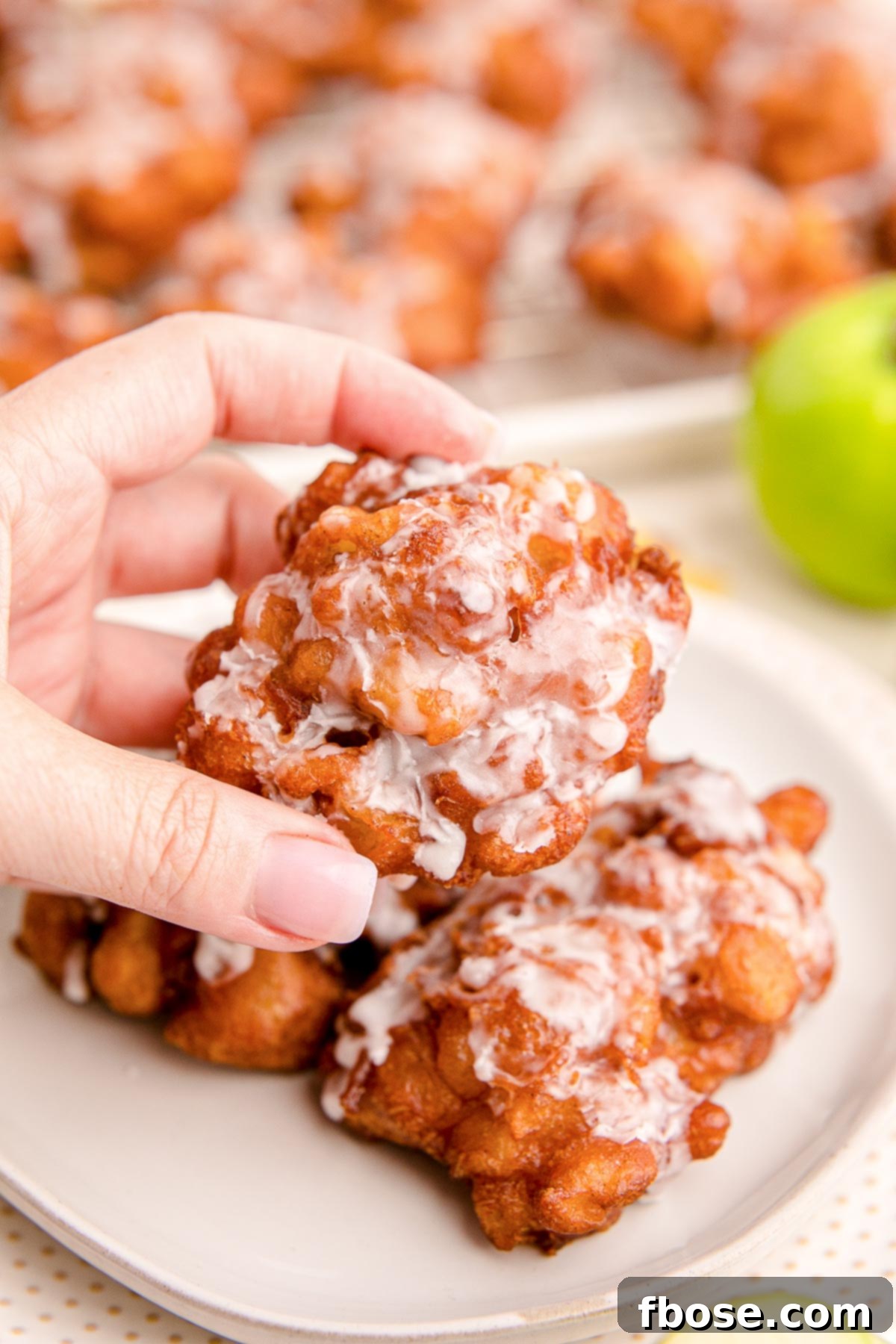 Close up photo of a woman's hand holding an apple fritter.