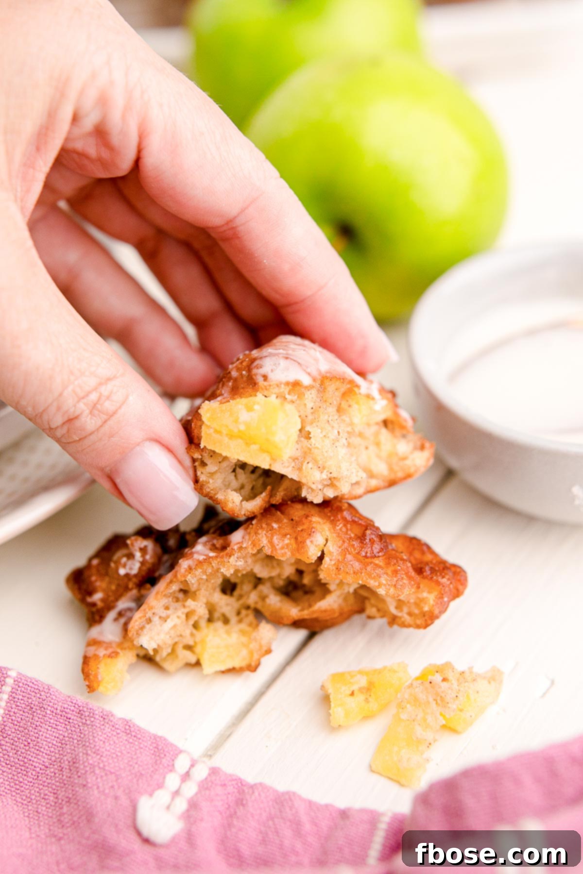 A woman's hand holding a piece of apple fritter that's been broken off to show the inside texture.
