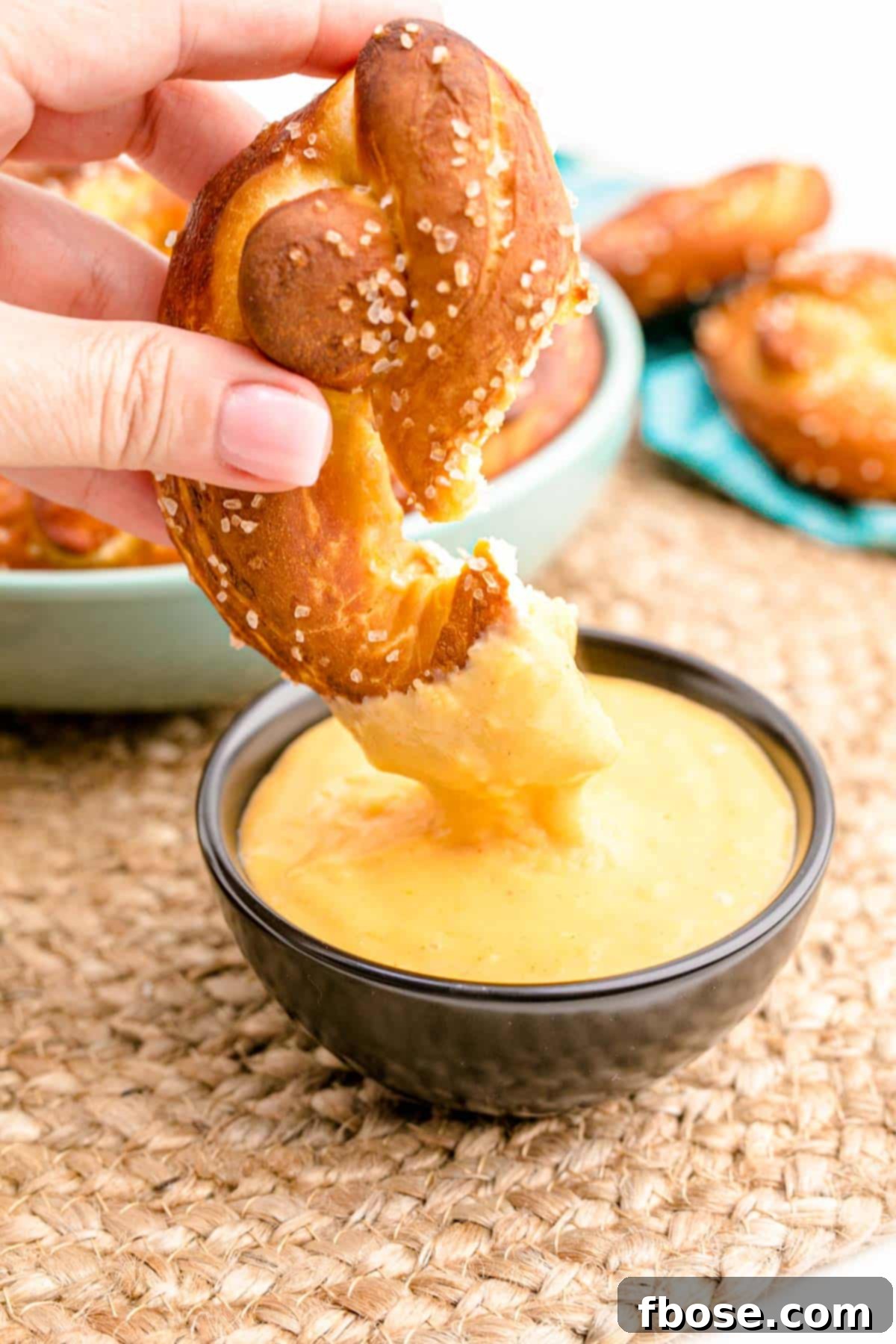 A woman's hand dipping a perfectly golden soft pretzel into a bowl of rich, creamy beer cheese dip.