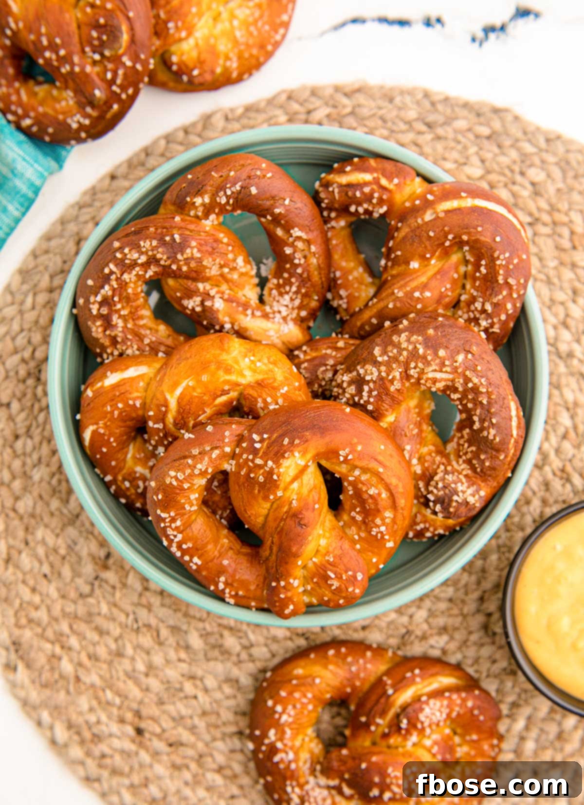 Overhead photo of a teal bowl filled with fresh homemade soft pretzels, placed on a woven placemat.