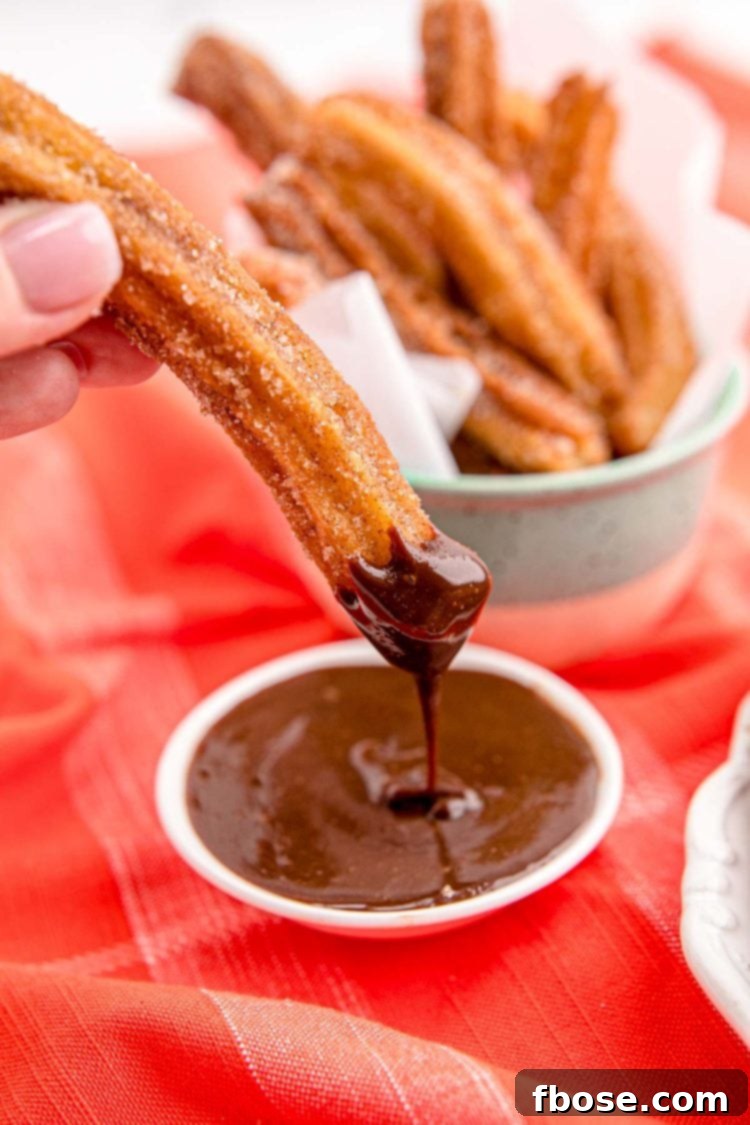 Close up photo of a woman's hand dunking a churro in chocolate sauce.