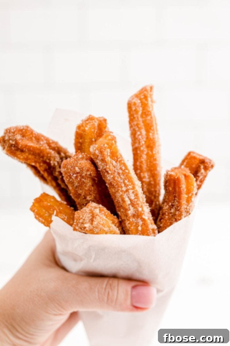 A woman's hand holding churros wrapped in parchment paper.