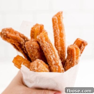A woman's hand holding churros wrapped in parchment paper.