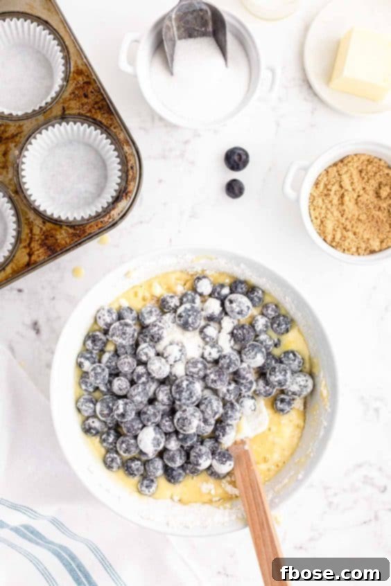Overhead photo of blueberries coated in flour being added to a mixing bowl with muffin batter.