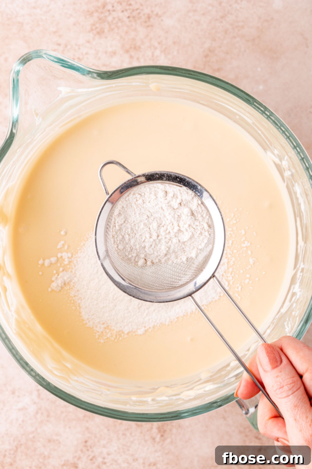 Flour being sifted into cheesecake mixture.