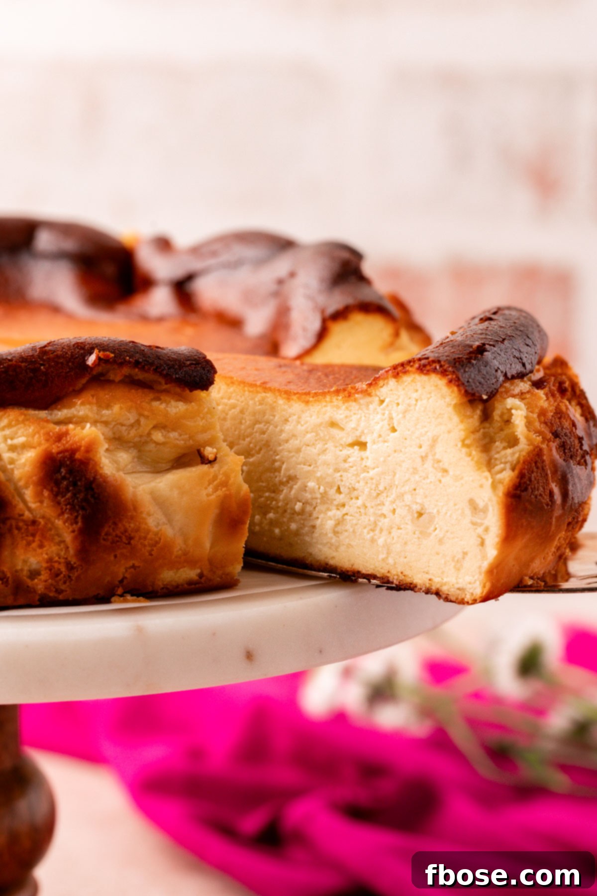 A slice of basque cheesecake being pulled from a cake stand.