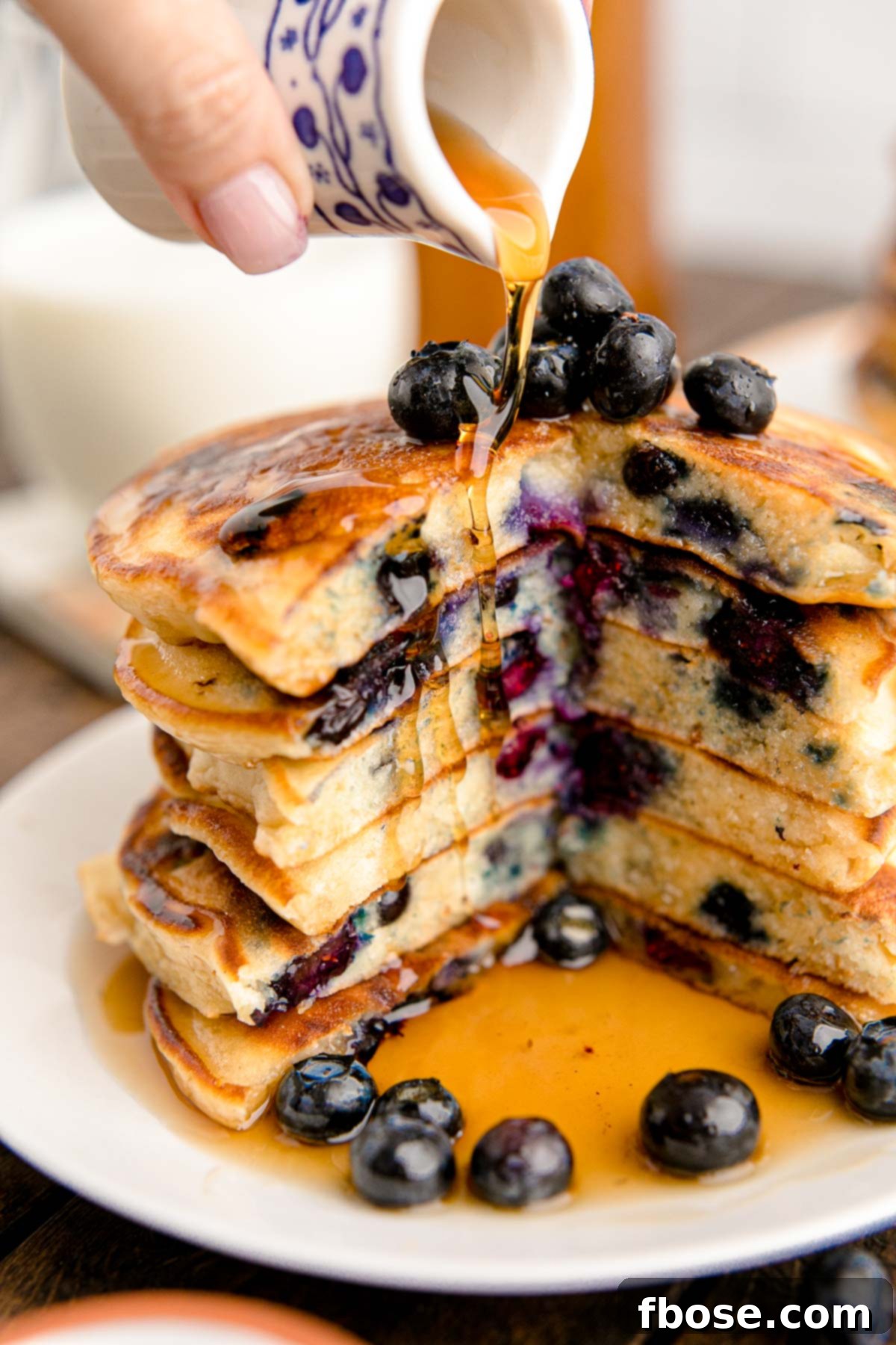 A stack of blueberry pancakes with a slice taken out of them getting more maple syrup poured on them.