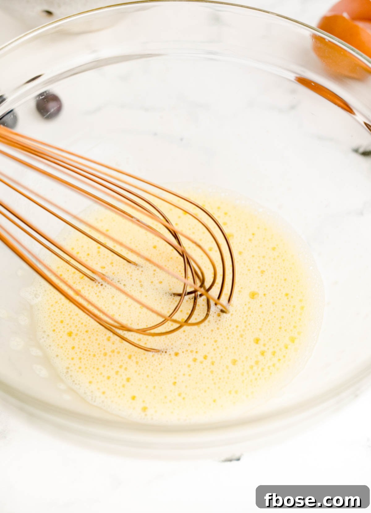 Egg being whisked in a glass mixing bowl.