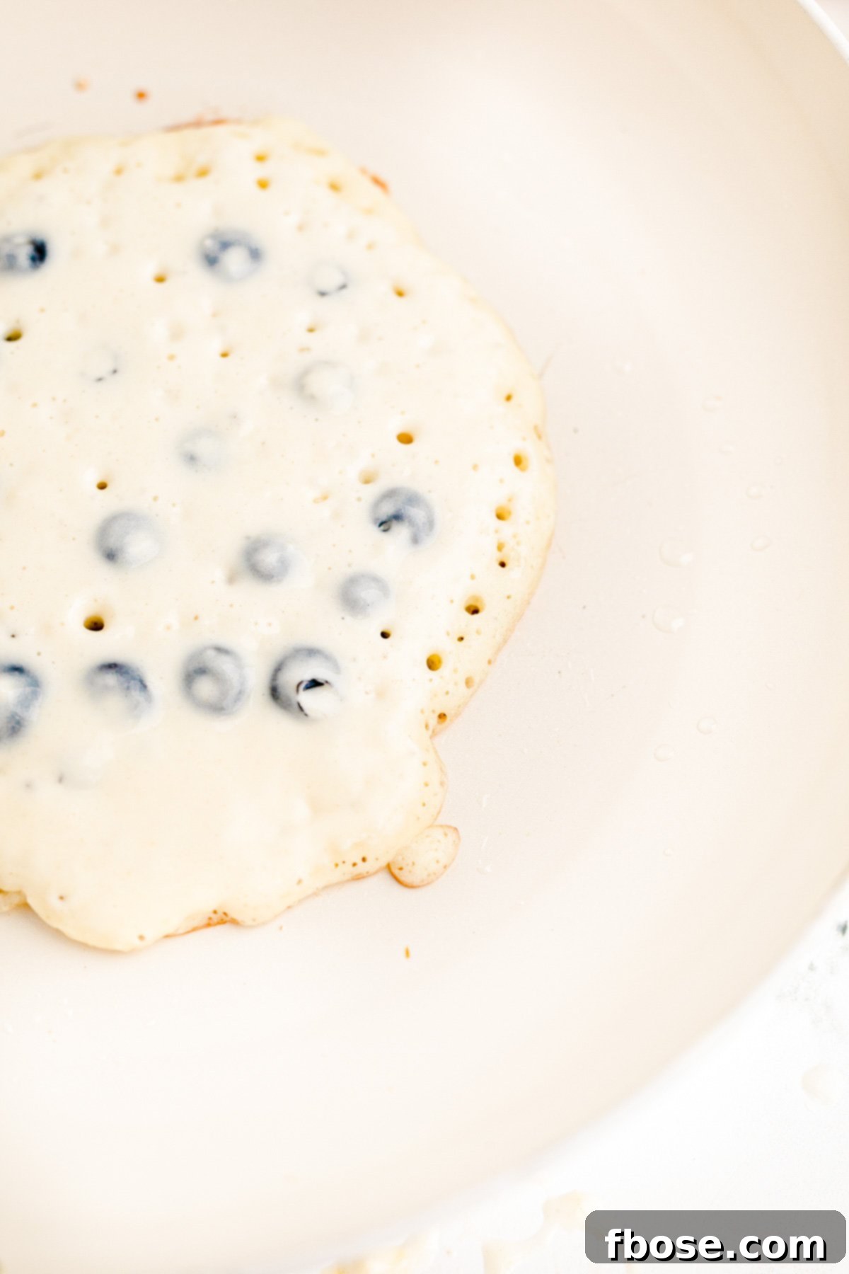 Close up photo of a blueberry pancakes being cooked in a white skillet.