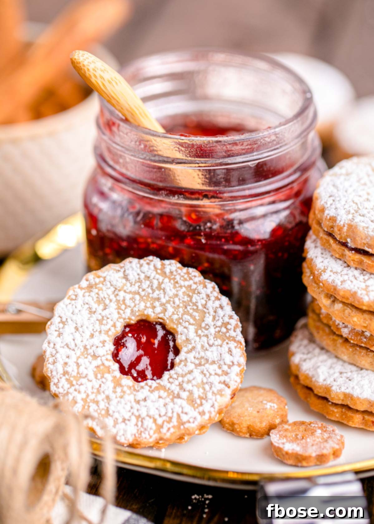 Berry-Filled Linzer Delights 2 Close up photo of linzer cookies on a plate next to a jar of raspberry jam.