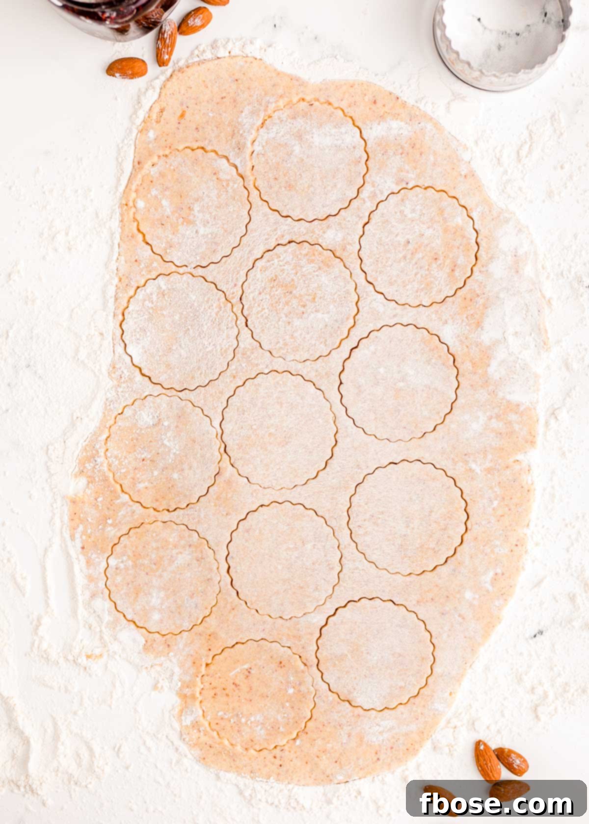 Berry-Filled Linzer Delights 11 Overhead photo of linzer cookie dough rolled out on a table with round cookies cut out of it.
