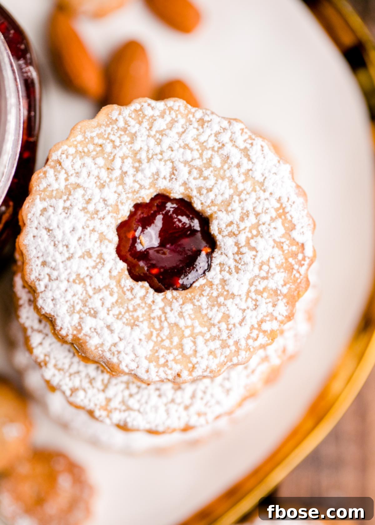 Berry-Filled Linzer Delights 15 Overhead photo of a stack of linzer cookies on a white plate with a gold trim.