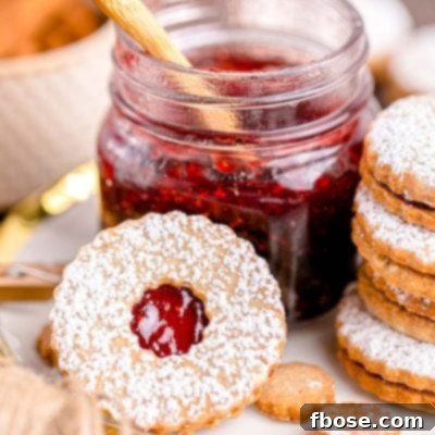 Close up photo of linzer cookies on a plate next to a jar of raspberry jam.