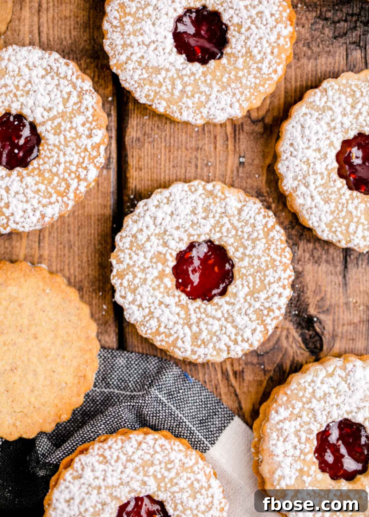 Berry-Filled Linzer Delights 3 Overhead photo of linzer cookies on a wooden table with a black and white napkin.