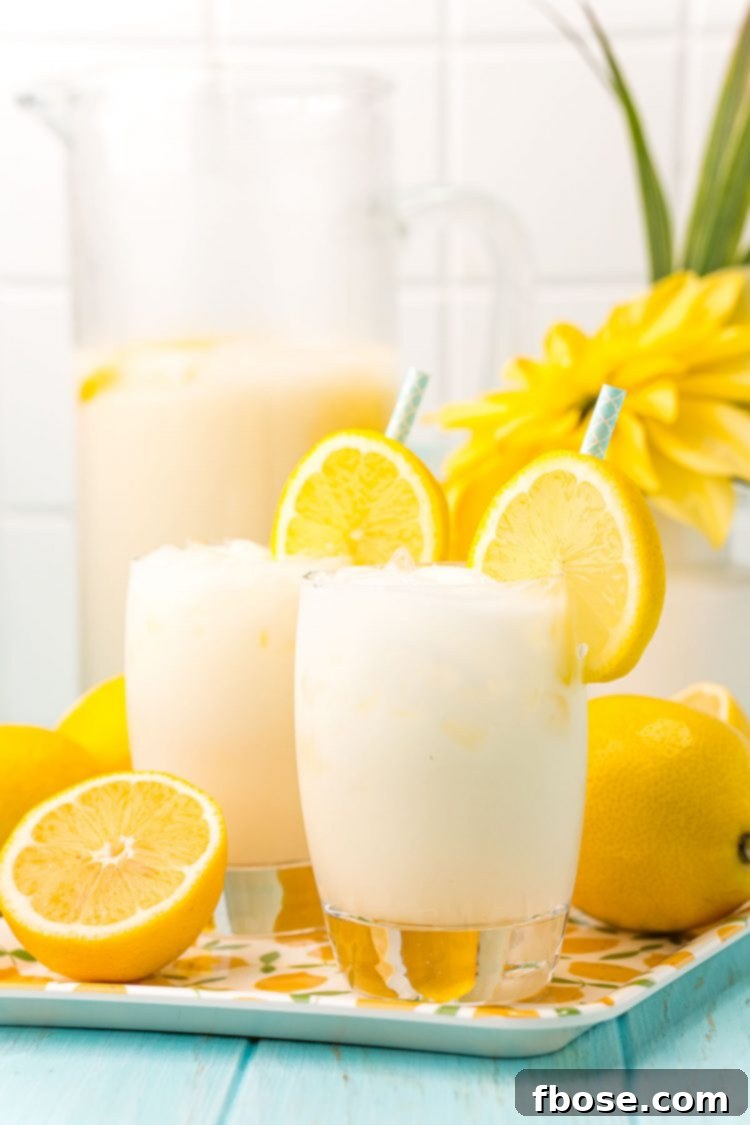 Straight on photo of two glasses of creamy lemonade on a tray with lemons and a pitcher in the background.