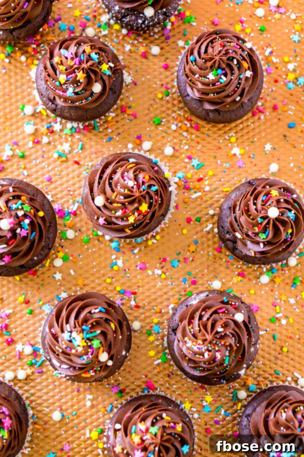 Freshly baked Chocolate Cupcakes arranged on a stylish copper baking sheet, with colorful sprinkles artfully scattered around, awaiting frosting.