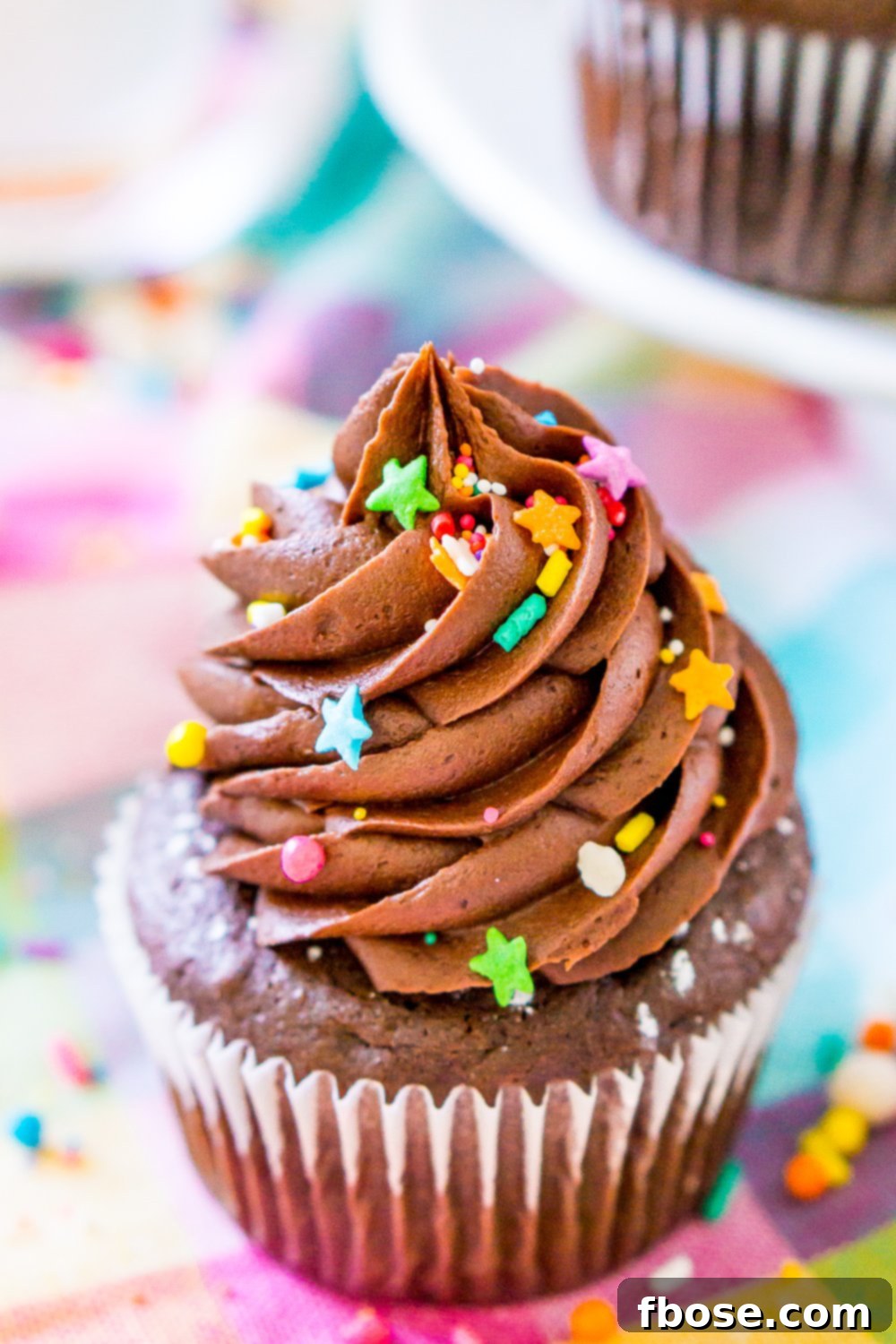 A single, beautifully frosted Chocolate Cupcake resting delicately on a vibrant, colorful napkin, showcasing its appealing texture and generous frosting.