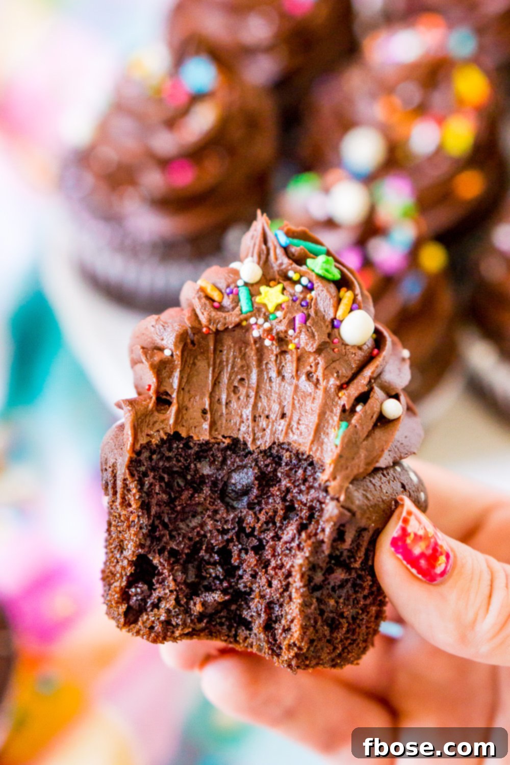 A woman's hand gently holding a delightful chocolate cupcake, from which a bite has been taken, revealing the moist cake inside.