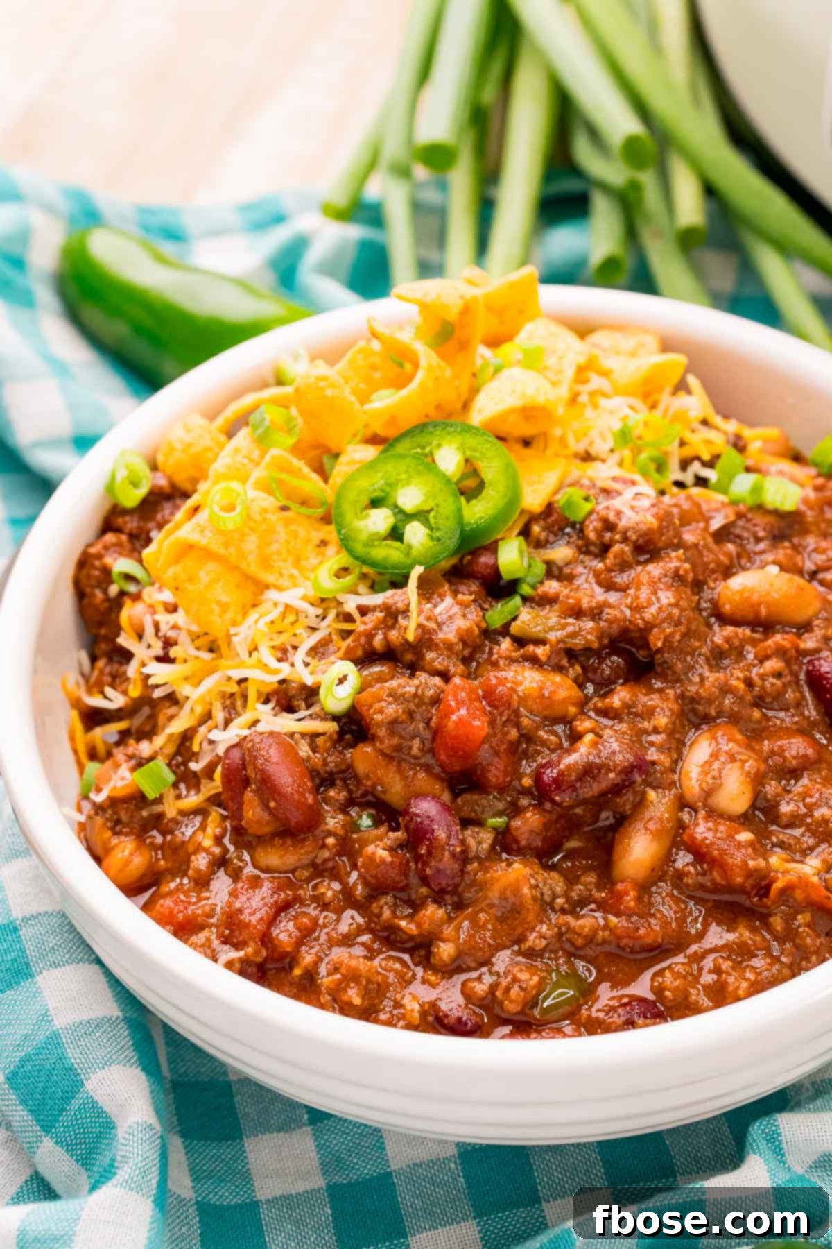Ultimate Slow Cooker Chili 6 Close-up photo of a comforting bowl of slow cooker chili, topped with fresh green peppers, resting on a gingham napkin with a blurred background.