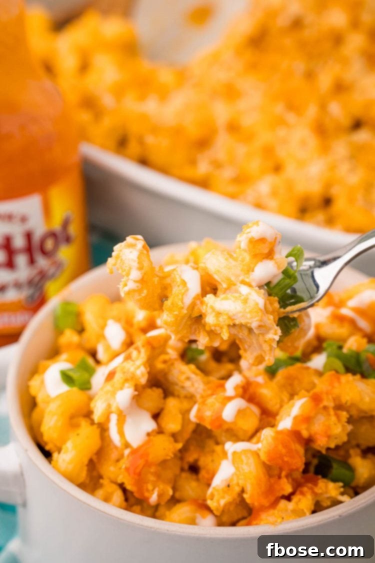 A fork taking a bite of buffalo mac and cheese out of a bowl.